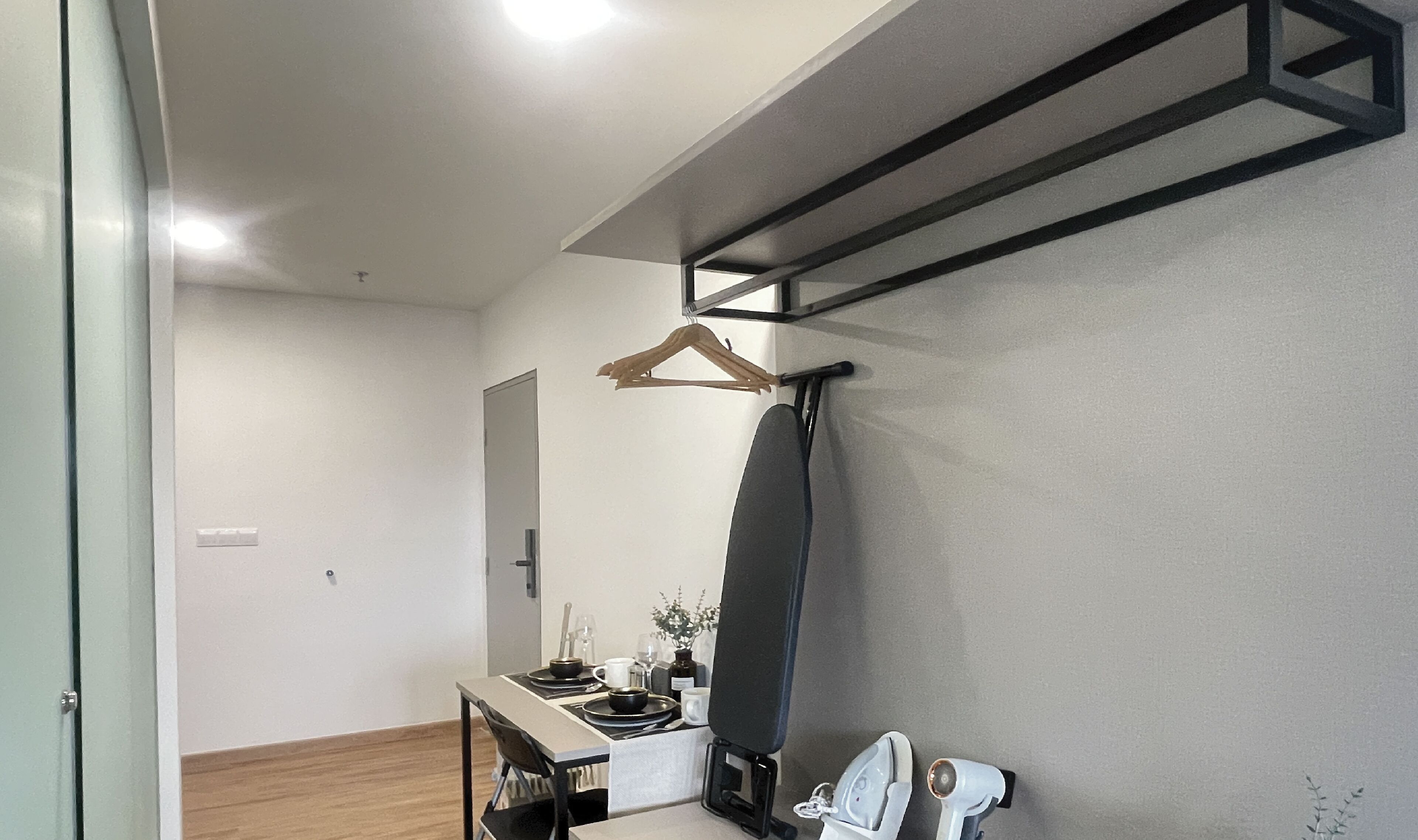 Una habitación moderna con diseño minimalista, que incluye un escritorio con silla, una percha para ropa y un espejo grande.