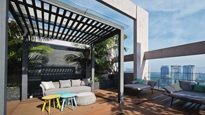 A modern outdoor patio with a wooden deck, a gray sofa, colorful chairs, and a pergola. - The Riv Riveria City KL Sentral (Kuala Lumpur)