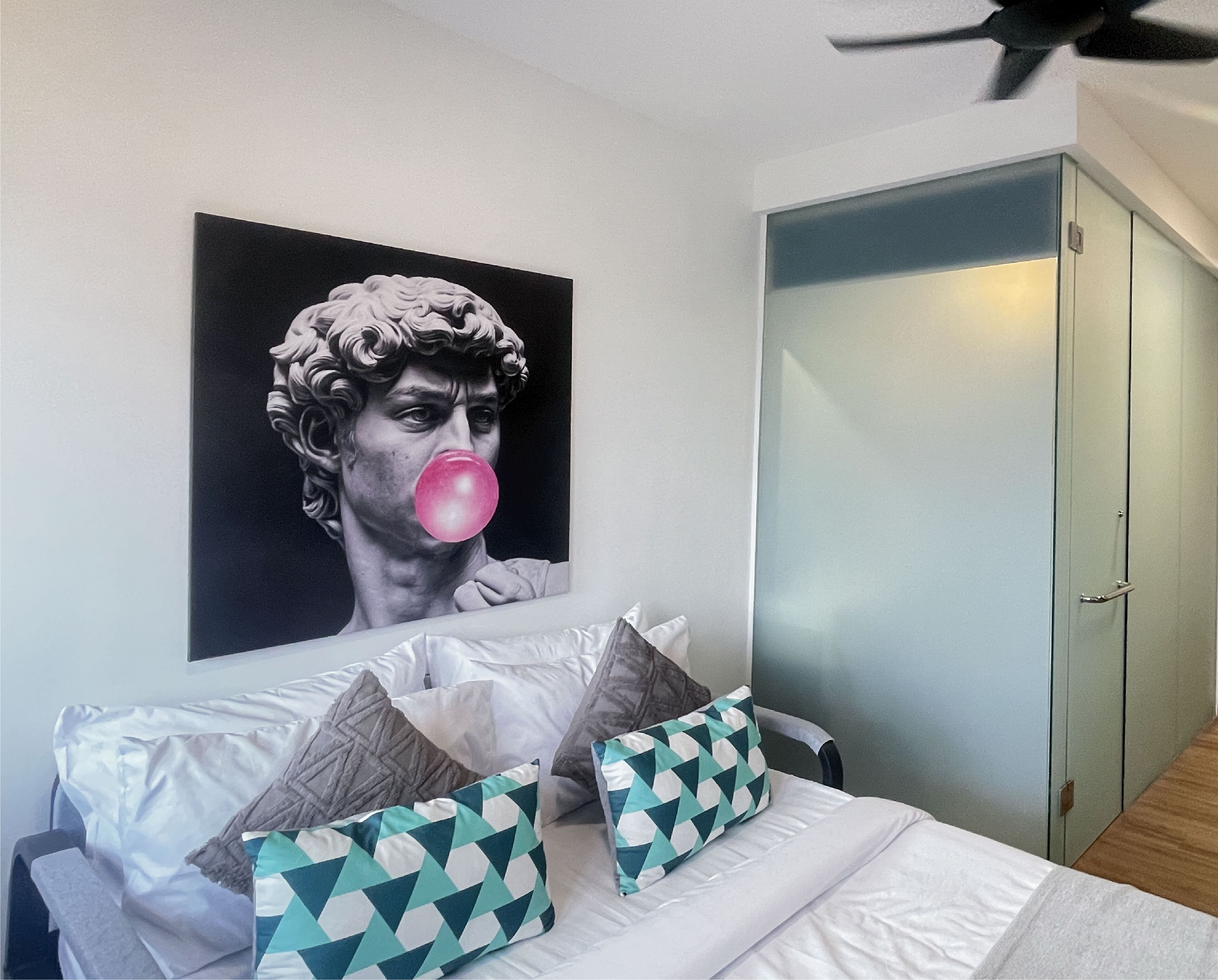 A bedroom with a bed, pillows, a wardrobe, and a wall-mounted artwork.