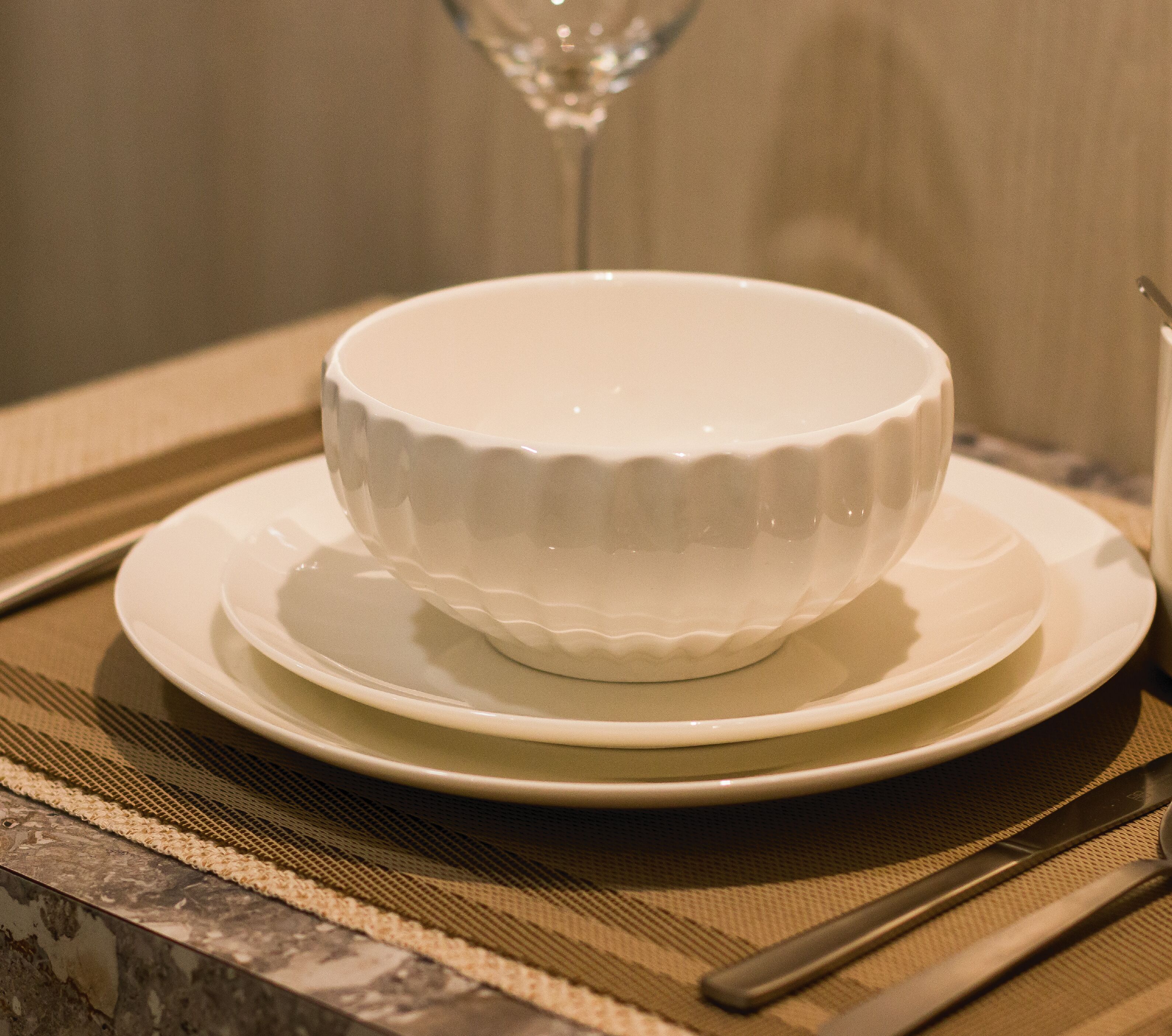 A white bowl on a plate, placed on a table with a woven placemat.