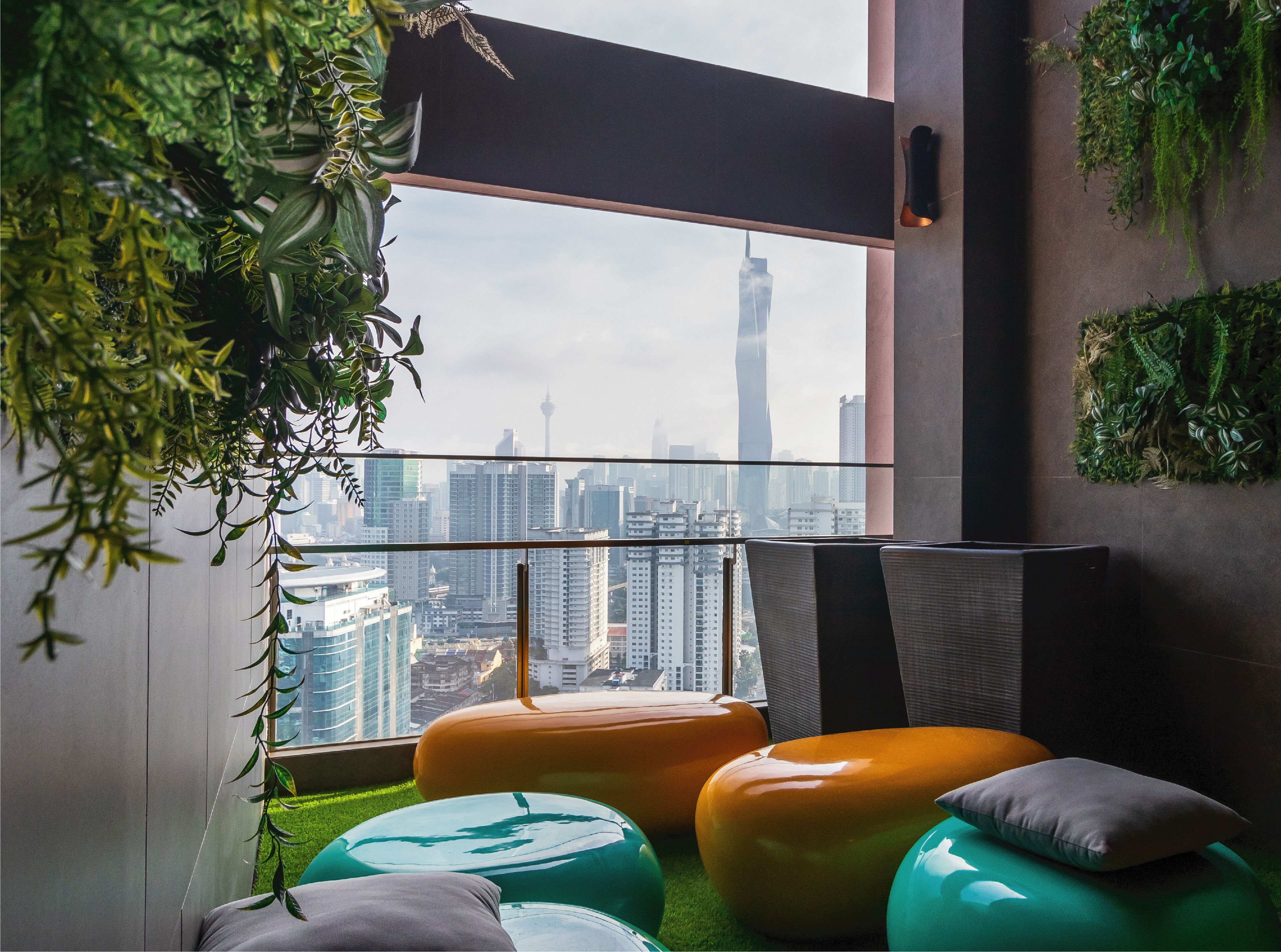 A modern room with a large window overlooking a cityscape, featuring green plants, a glass railing, and colorful seating.