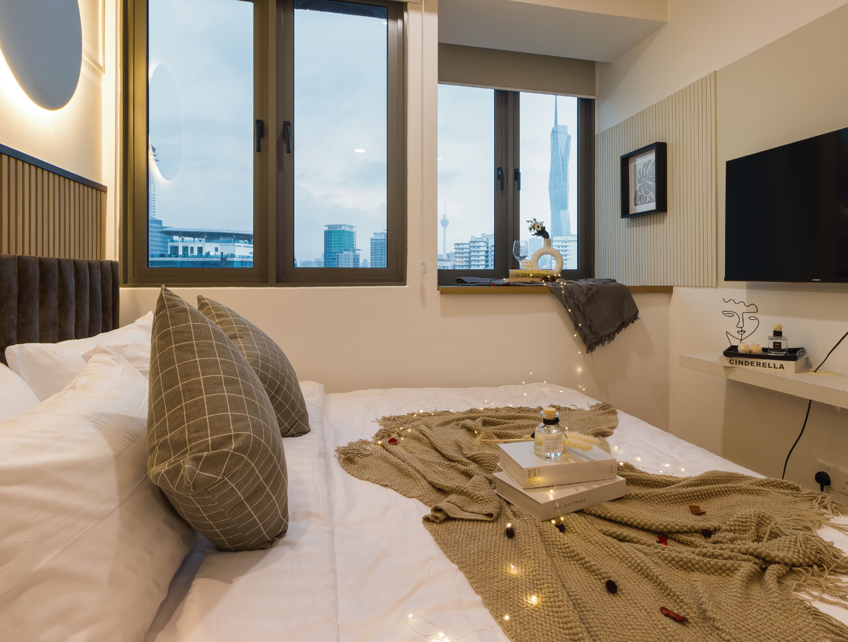 Habitación de hotel moderna con una cama grande, un ventanal con vistas a la ciudad, un televisor montado y una estantería con un adorno.