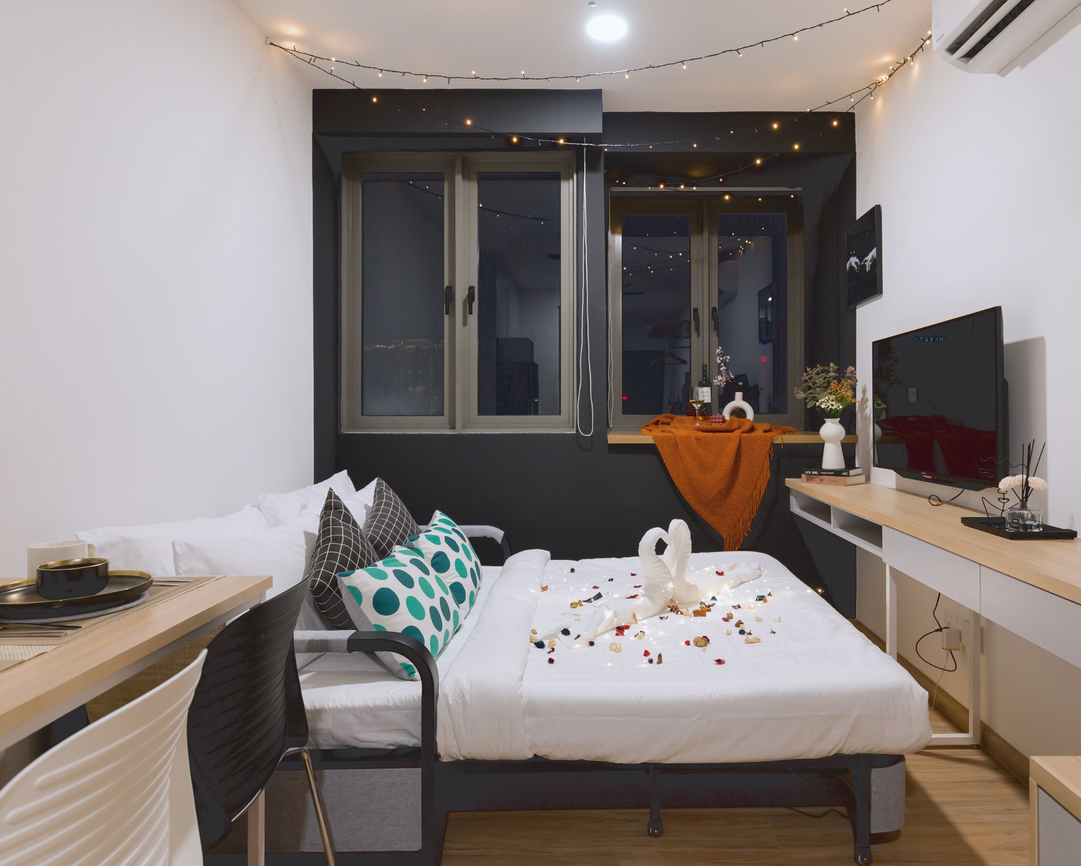 A modern bedroom with a bed, a desk, a TV, and a window with curtains.