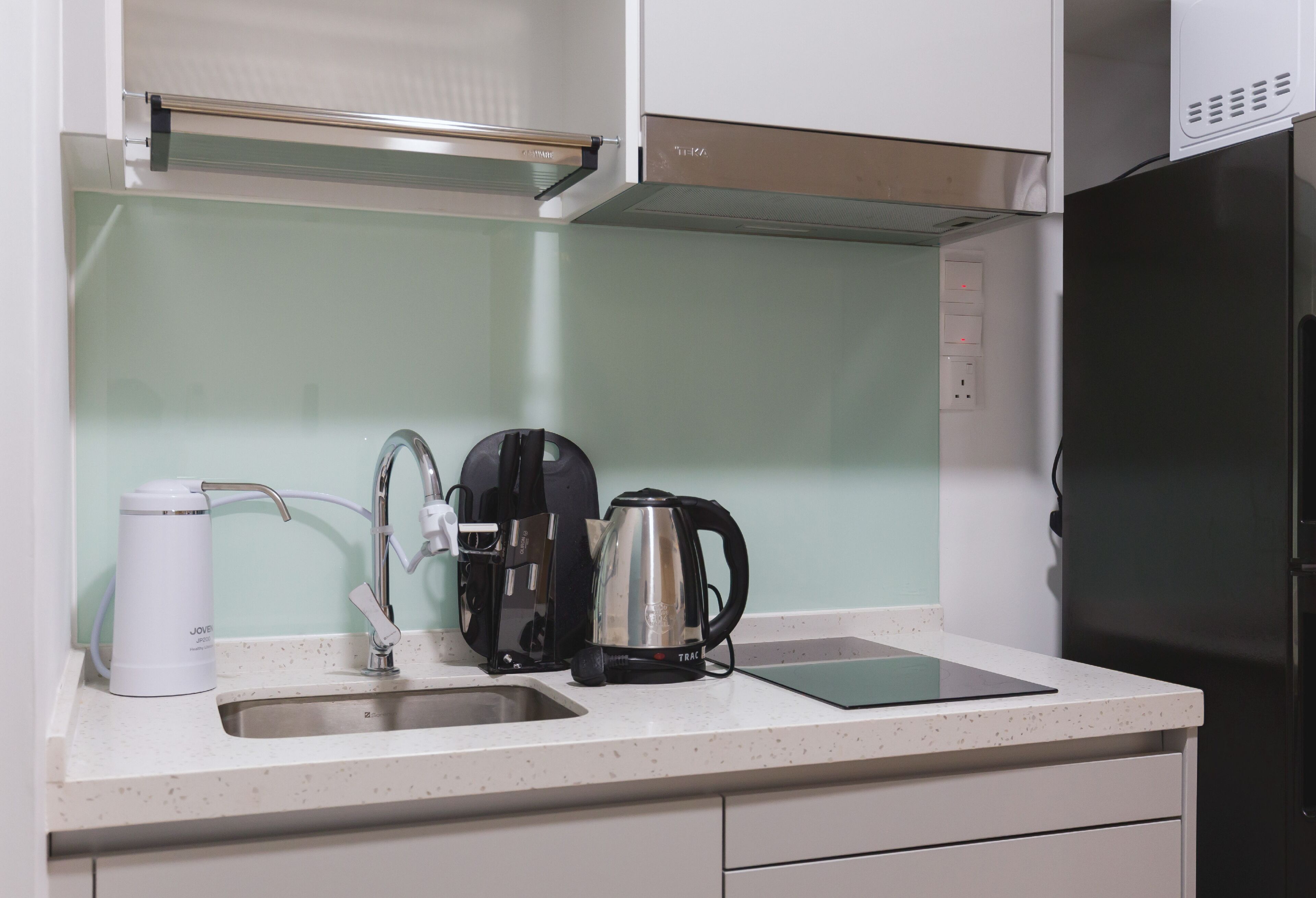 Una cucina con lavello in acciaio inox, una macchina da caffè, un bollitore e un frigorifero nero.