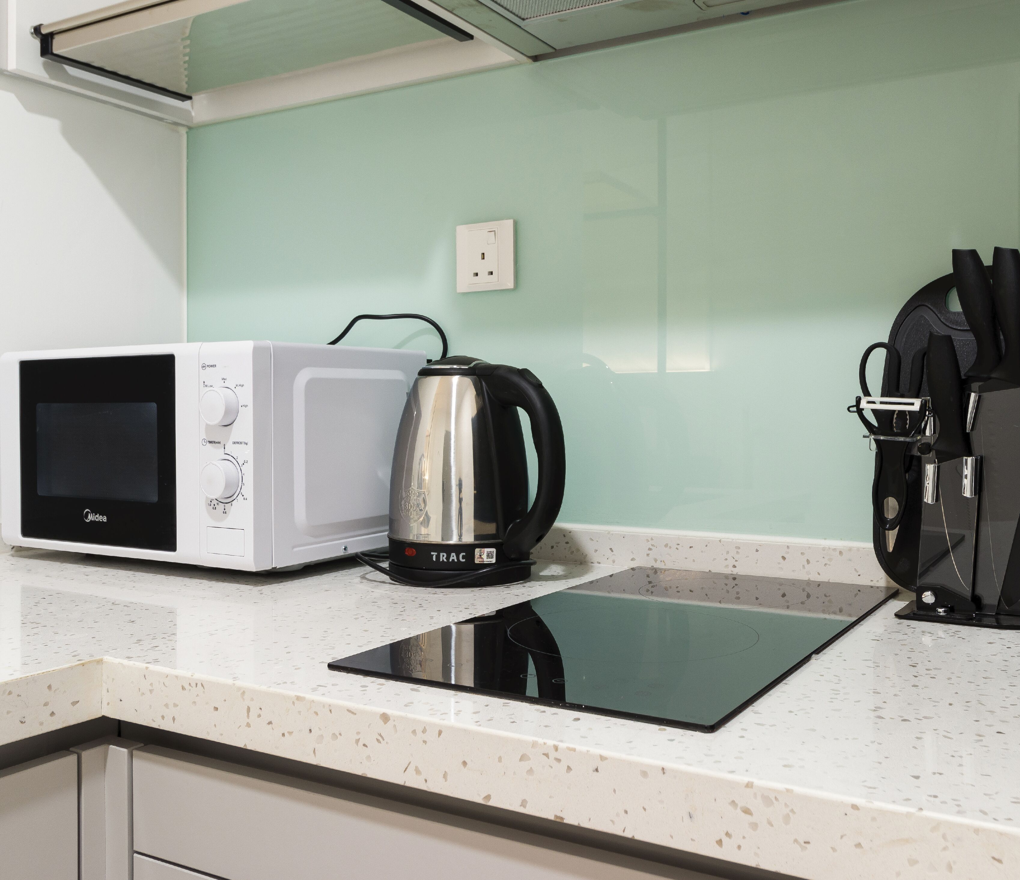 A kitchen with a microwave, a kettle, and a coffee machine on a countertop.