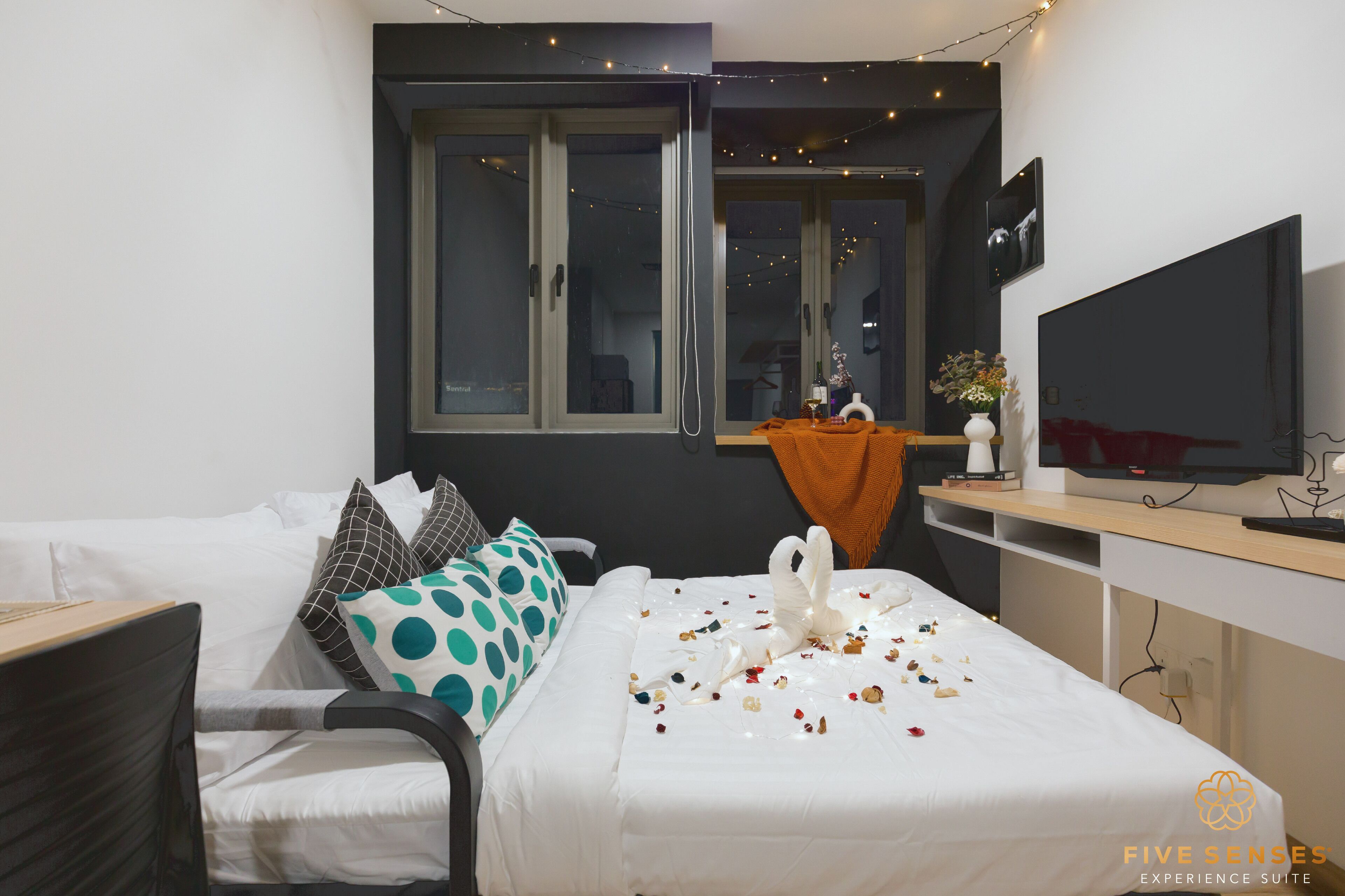 Une chambre d’hôtel avec un lit, une télévision, une fenêtre avec des rideaux et une petite table sur laquelle se trouve un vase.