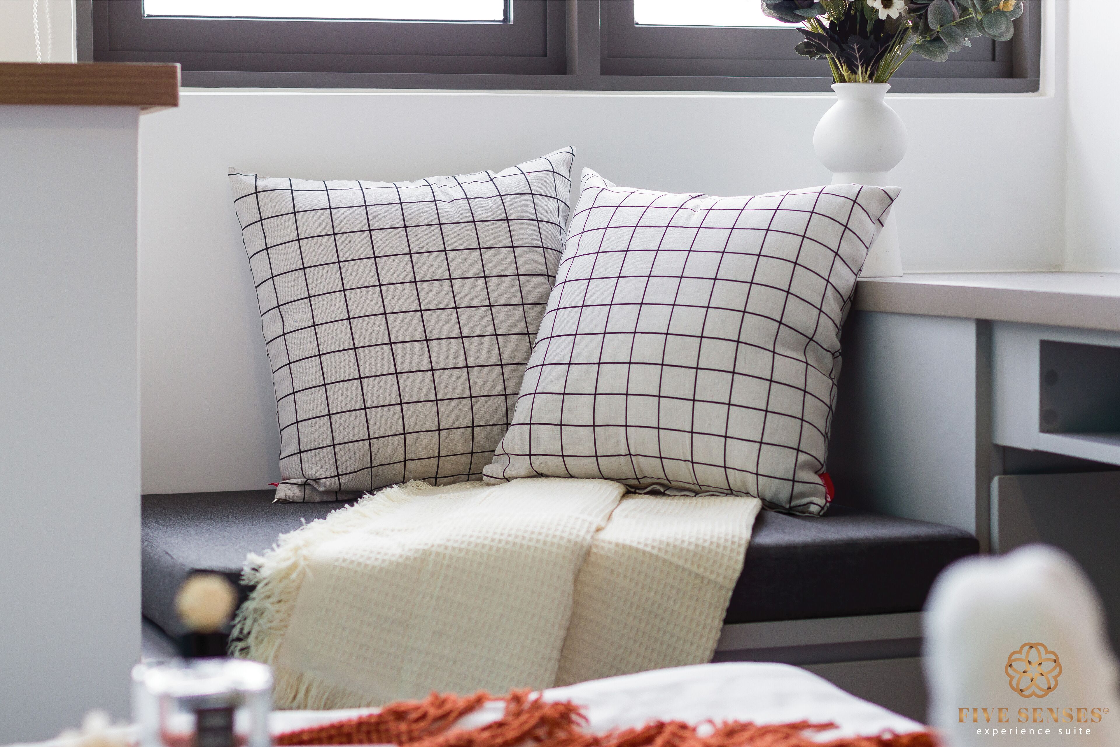 A modern room with a window seat featuring two checkered pillows and a white throw blanket.