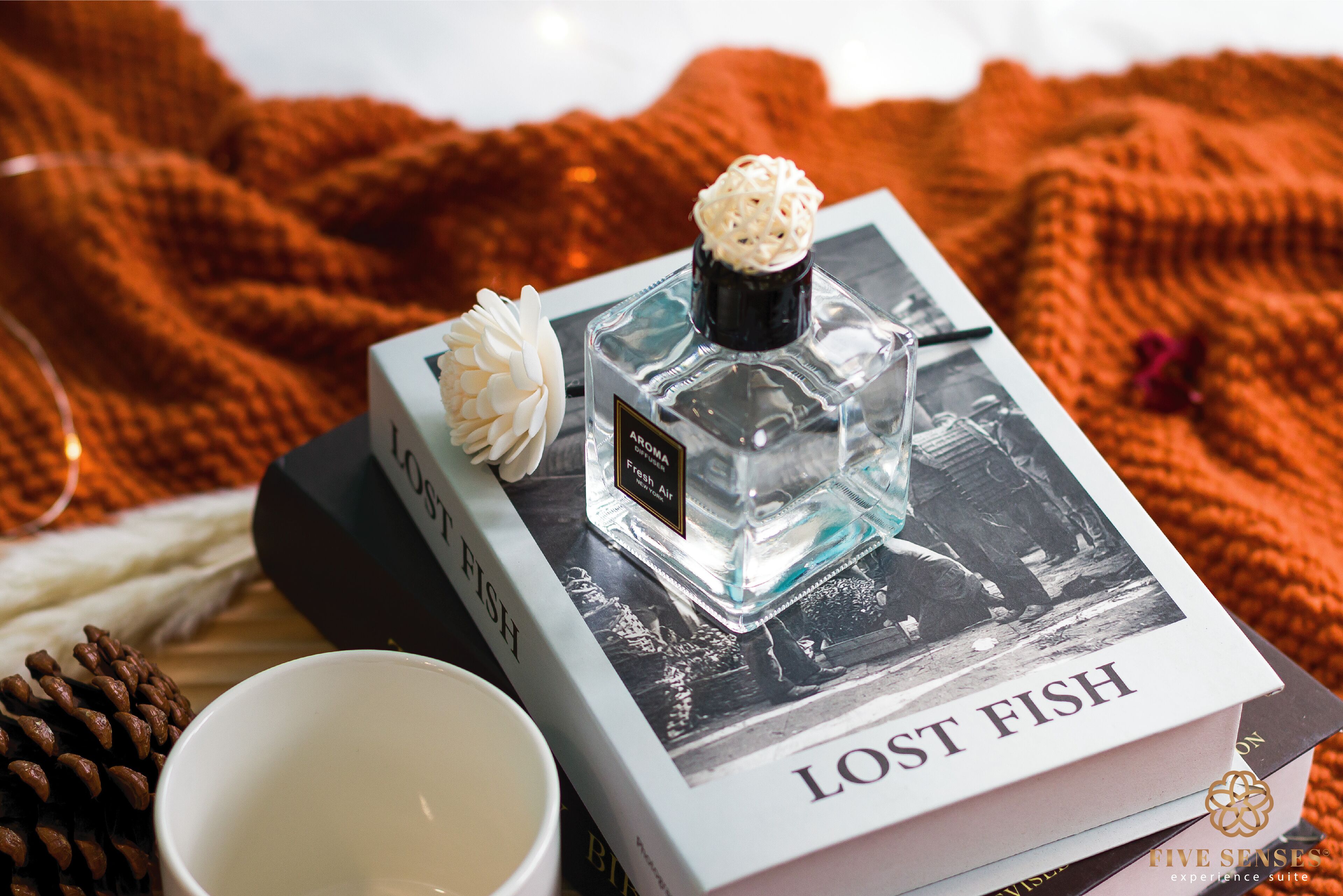 A book titled 'Lost Fish' with a perfume bottle on top, a white flower, and a white cup beside it.