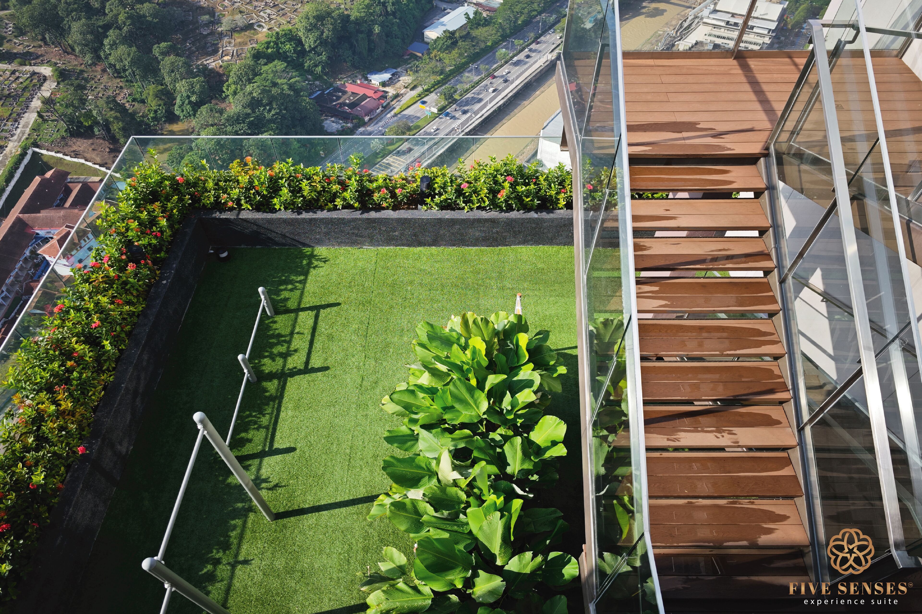 A rooftop garden with a glass balustrade, a wooden staircase, and a view of the cityscape.