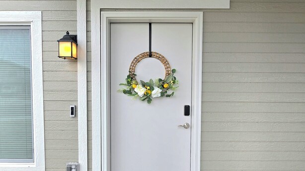 A front door with a wreath, a doormat, and a wall-mounted light fixture. - Eastern Desert Chic (Umatilla)