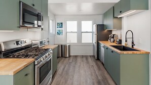 A modern kitchen with green cabinets, stainless steel appliances, a wooden countertop, and a window with white frames. - NordEast Escape/Hot Tub, Bocce court, Fooseball, Patio, Awesome location (Minneapolis)
