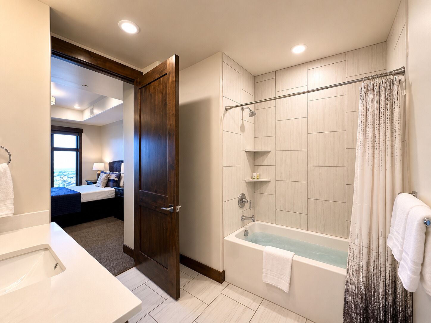 Une salle de bain d’hôtel avec une baignoire, une douche et un lit visible dans la pièce adjacente.