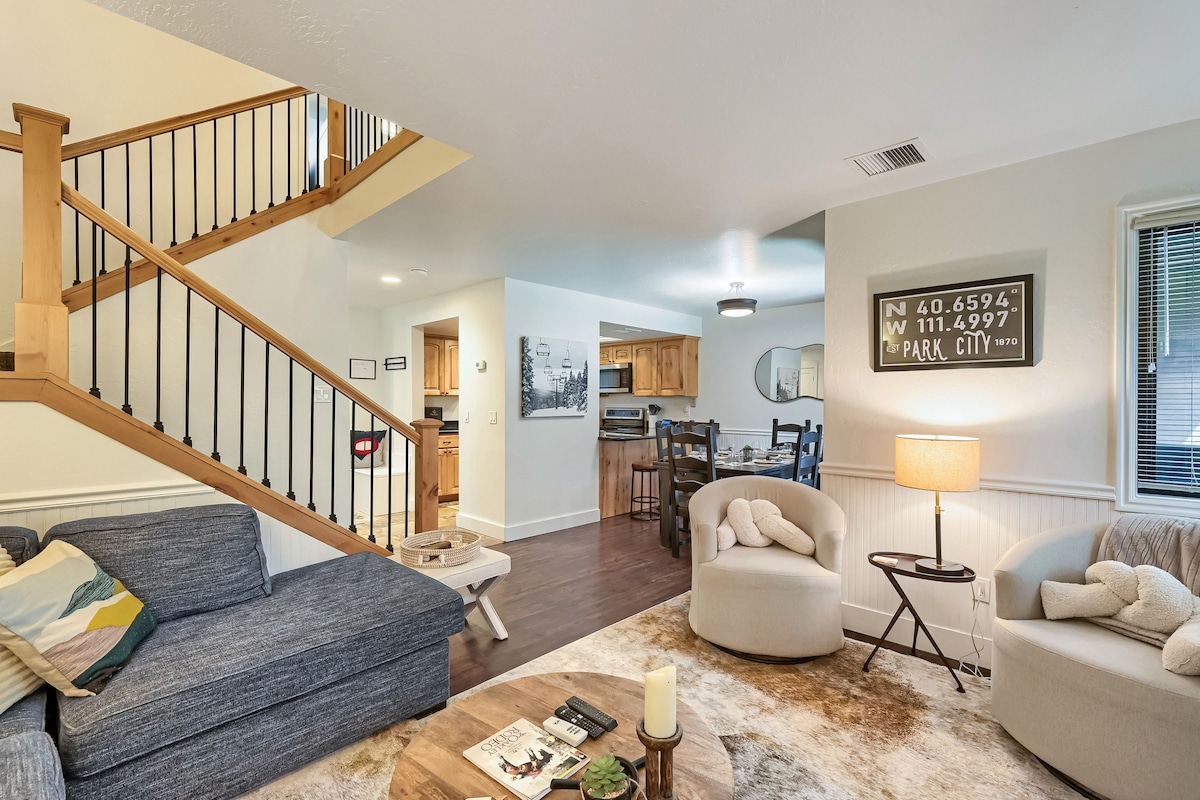 A spacious living area with a wooden staircase, a dining area, and a kitchen.