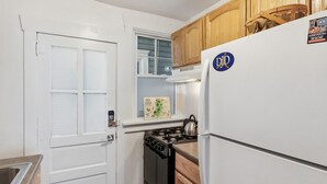 A compact kitchen with white cabinetry, a stove, a refrigerator, and a window with blinds.