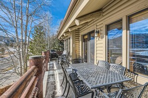 Une cabane en bois dotée d’un patio avec une table et des chaises, de grandes fenêtres et une vue sur un paysage enneigé.