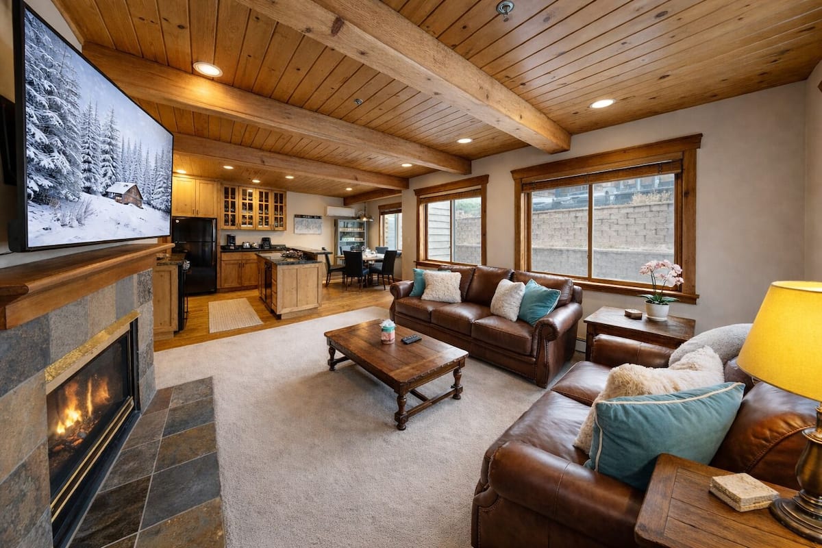 A cozy living room with a fireplace, leather sofa, and a dining area in the background.