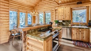A wooden cabin kitchen with a central island, large windows, and a stone fireplace. - Deer Valley Escapes - Park City Ski Resort Condos (Park City)