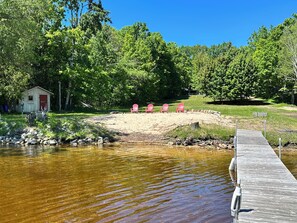 A wooden dock extending into a calm body of water, surrounded by lush greenery and a small shed with a red door.