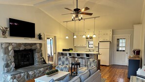 A living room with a stone fireplace, a grey sofa, and a TV mounted on the wall. - Private beachfront cottage,  WiFi and AC on Lake Paradise, minutes from Mackinaw (Carp Lake)