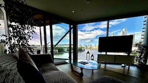 Ein modernes Wohnzimmer mit großem Fenster, einer Couch, einem Couchtisch und einem Fernseher.