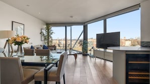 Ein modernes Wohnzimmer mit einem Glastisch, Sofas, einem Fernseher und Blick auf die Stadt.