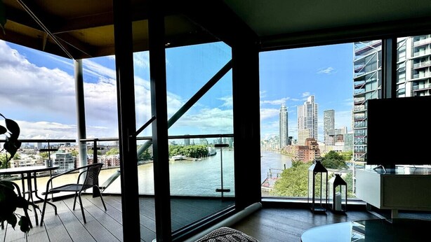 Ein modernes Wohnzimmer mit einem großen Fenster mit Blick auf einen Fluss und eine Stadtlandschaft.