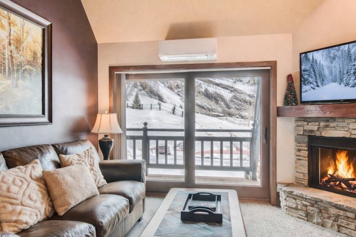 Ein gemütliches Wohnzimmer mit einer Ledersofa, einem Couchtisch, einem Kamin und einem großen Fenster mit Blick auf Schnee.
