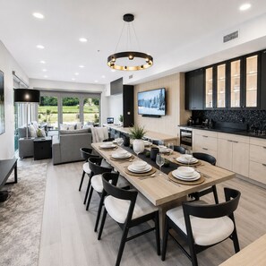 A modern kitchen with a dining area, a TV mounted on the wall, and a view of the outdoors.