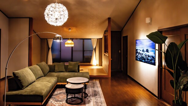 Een moderne woonkamer met een modulaire bank, een ronde salontafel, een vloerlamp en een groot televisiescherm.