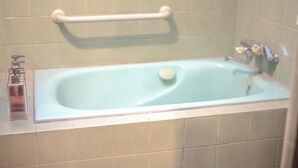 Een badkamer met een bad, een handgreep en een zeepdispenser.
