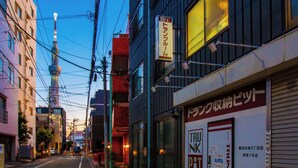 Straatbeeld met een gebouw met een bord met Japanse tekst, een zichtbare toren op de achtergrond en een winkel met een bord in het Engels.