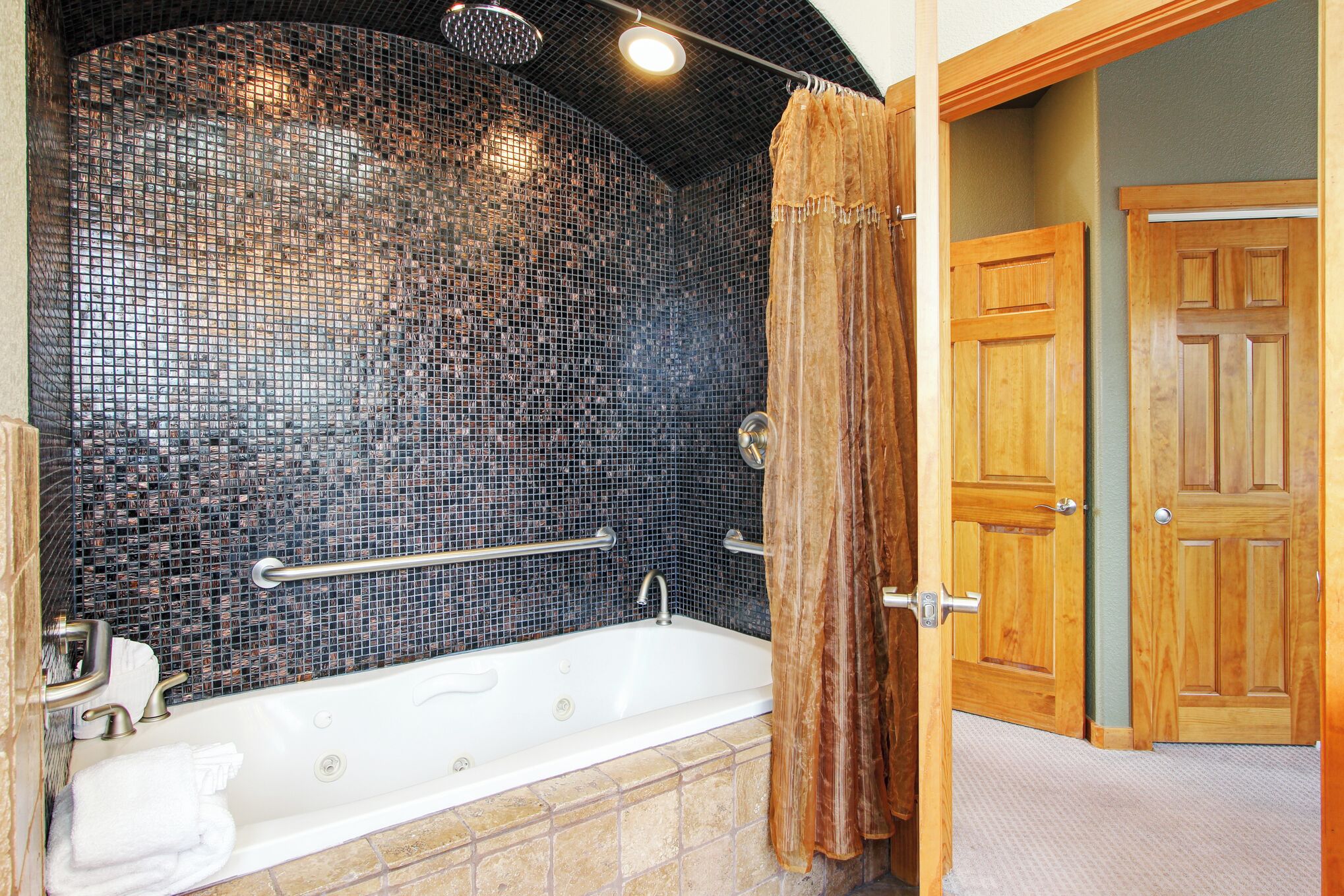 Un baño con pared de mosaicos, bañera, puertas de madera y cortina de ducha.