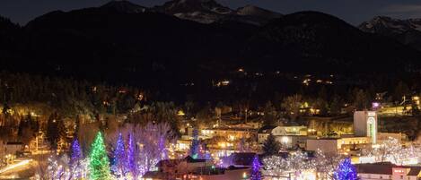 A town with illuminated Christmas trees and a mountain backdrop.