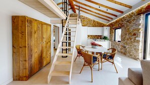 Ein modernes Interieur mit einer Holztreppe, Steinwänden und einem Essbereich mit Korbstühlen.