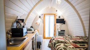 Une pièce confortable et compacte, dotée d’une kitchenette, d’un lit avec une couette, d’un plafond en bois et d’une petite fenêtre.