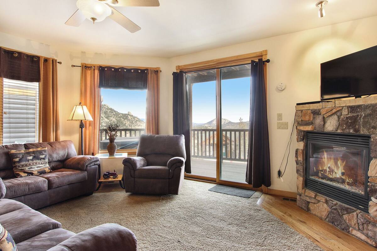 A living room with a fireplace, leather sofas, a stone fireplace surround, and a large window with a view of mountains.