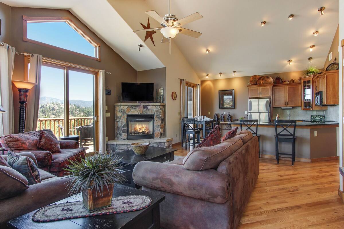 A spacious living area with a fireplace, comfortable seating, and a kitchen area with wooden cabinets and a bar.
