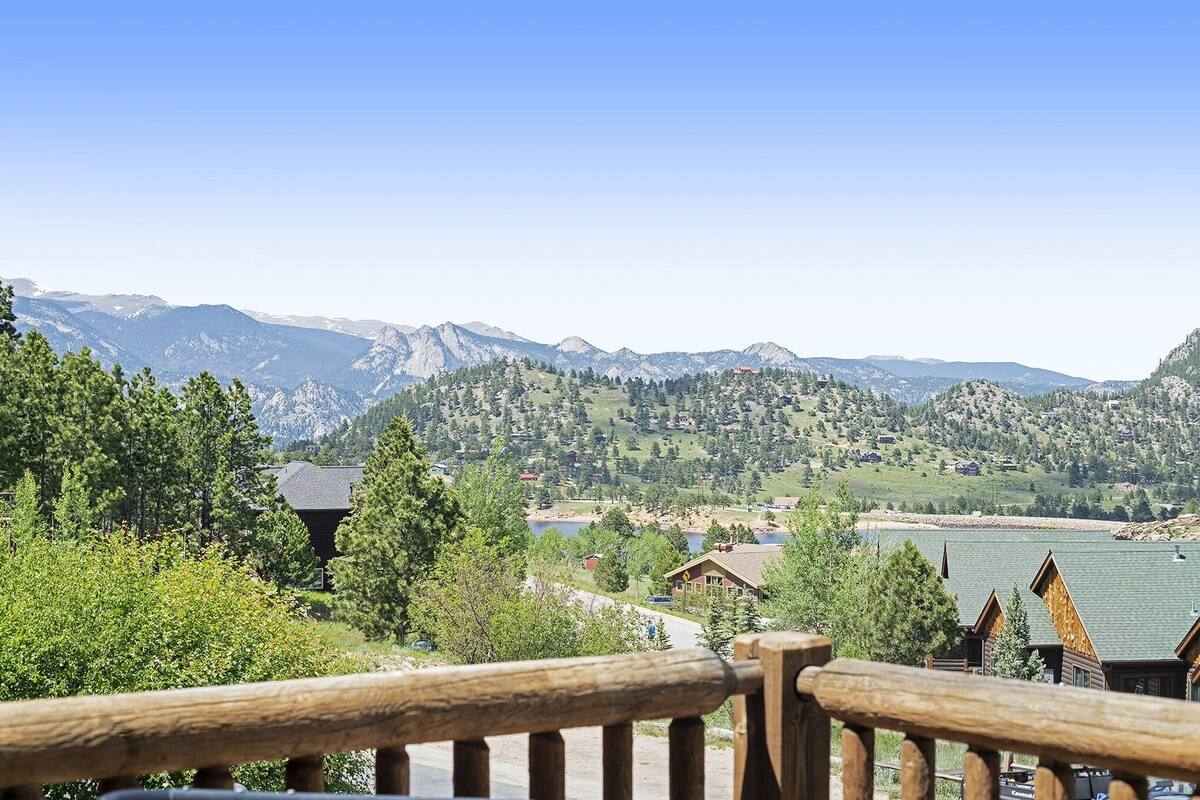 A mountain view with a wooden railing, houses, and a lake.