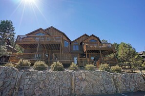 Situated among pine trees, this cabin features multiple balconies and large windows, with a stone wall bordering the property.