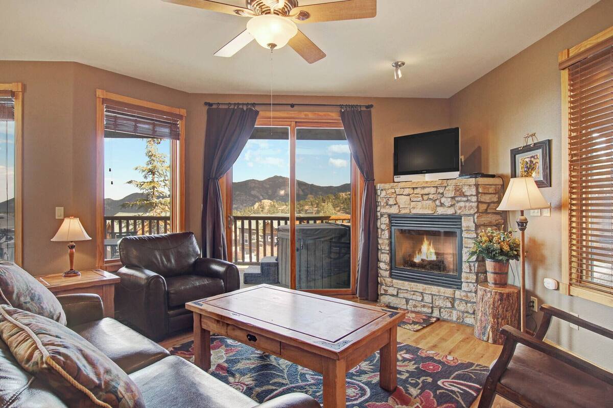 A cozy living room with a fireplace, leather sofa, and a large window with a view of mountains.