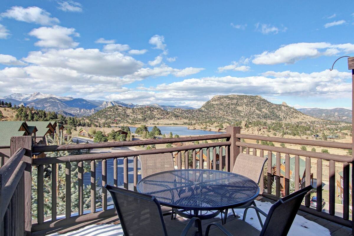 A balcony with a table and chairs overlooking a mountainous landscape and a lake.