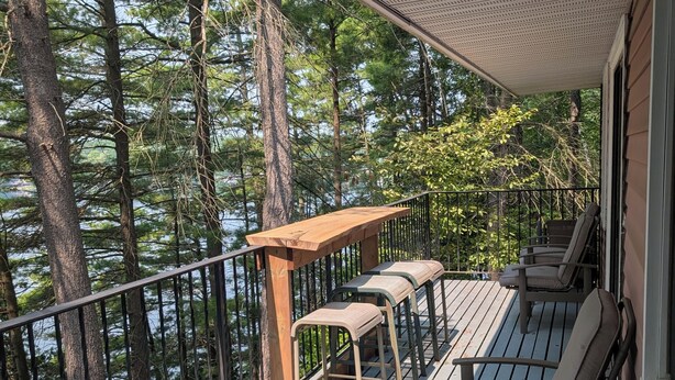 Une terrasse couverte, dotée de bancs en bois et d’une table, qui offre une vue sur une étendue d’eau bordée de grands arbres.