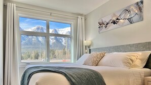 Een slaapkamer met een bed, een raam met uitzicht op de bergen, een lamp en een schilderij aan de muur.
