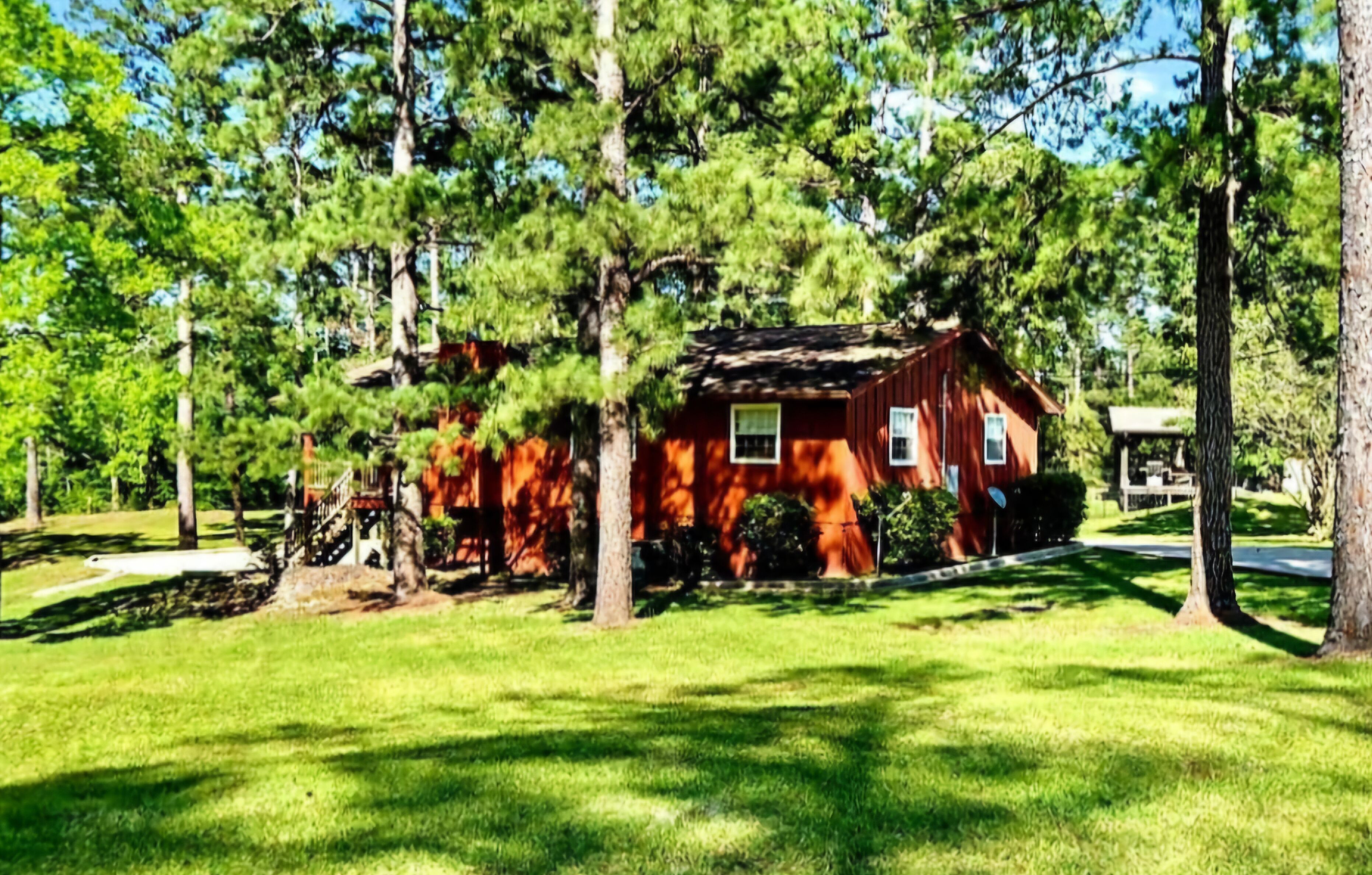 A rustic cabin surrounded by tall pine trees, with a well-maintained lawn and a small porch.