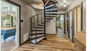 Un escalier en colimaçon dans un couloir, avec un plancher en bois, une table de billard et une commode.