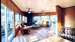 Un vaste salon doté d’une cheminée, de grandes fenêtres et d’une terrasse en bois.