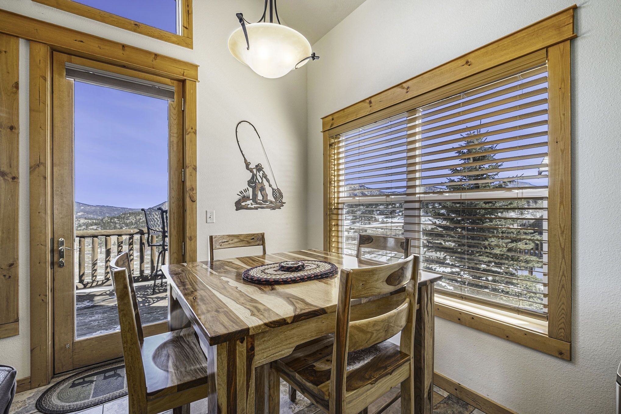 A wooden dining table with chairs, a pendant light, a wall-mounted sculpture, and a window with blinds.