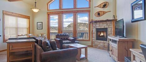 A spacious living room with a fireplace, large windows, a pool table, and a cozy seating area.