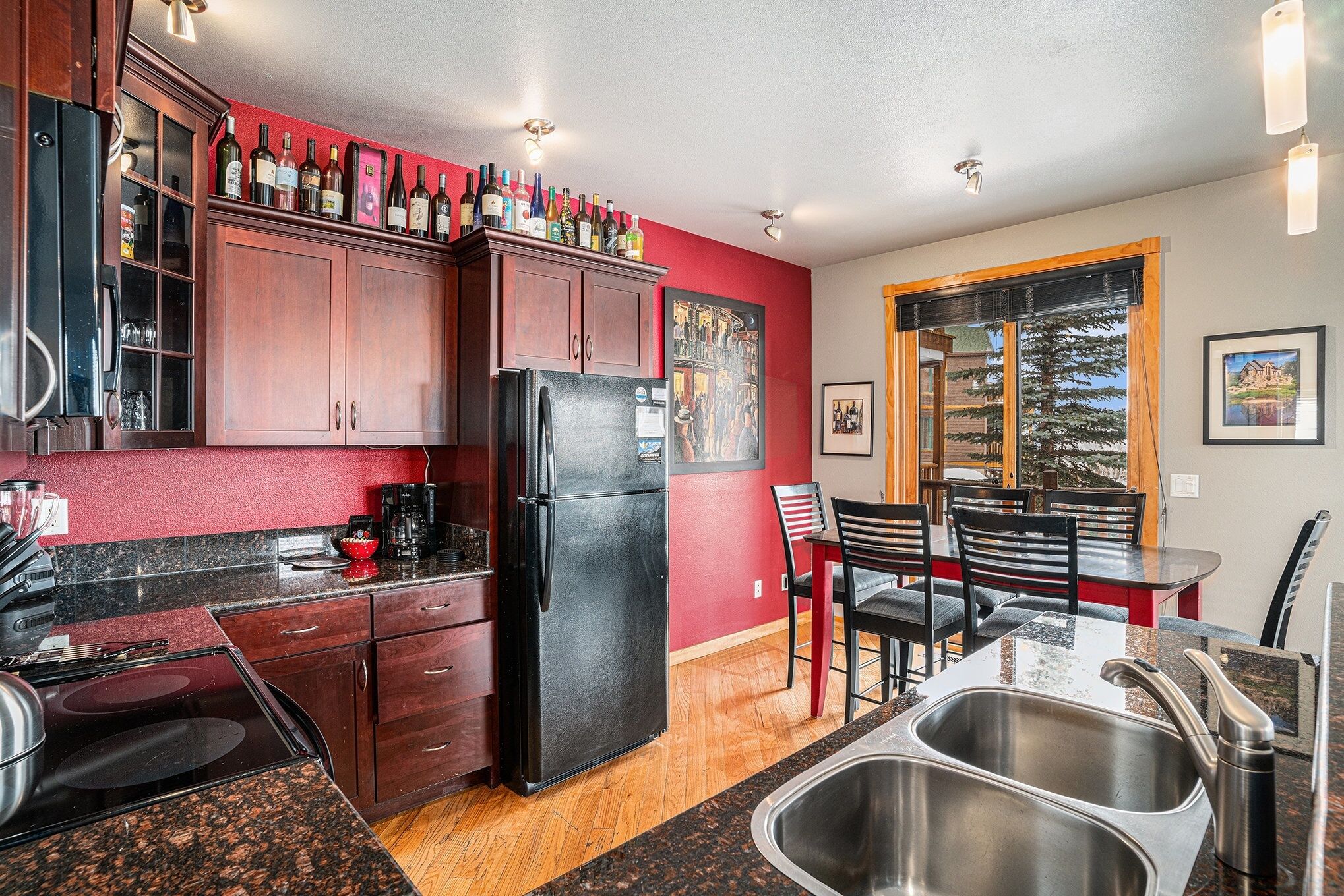 A kitchen with dark wooden cabinets, a black refrigerator, and a dining area with a table and chairs.