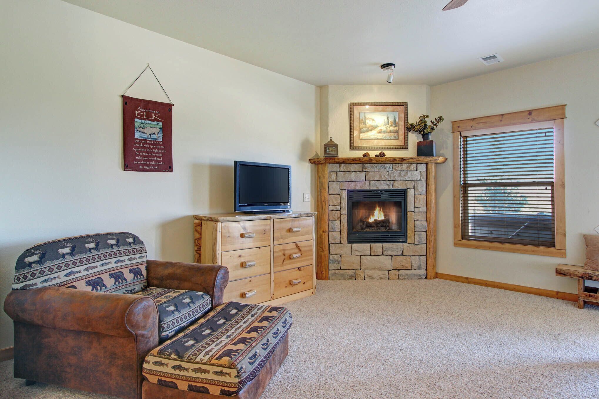 A living room with a stone fireplace, a television on a wooden cabinet, and a patterned sofa.
